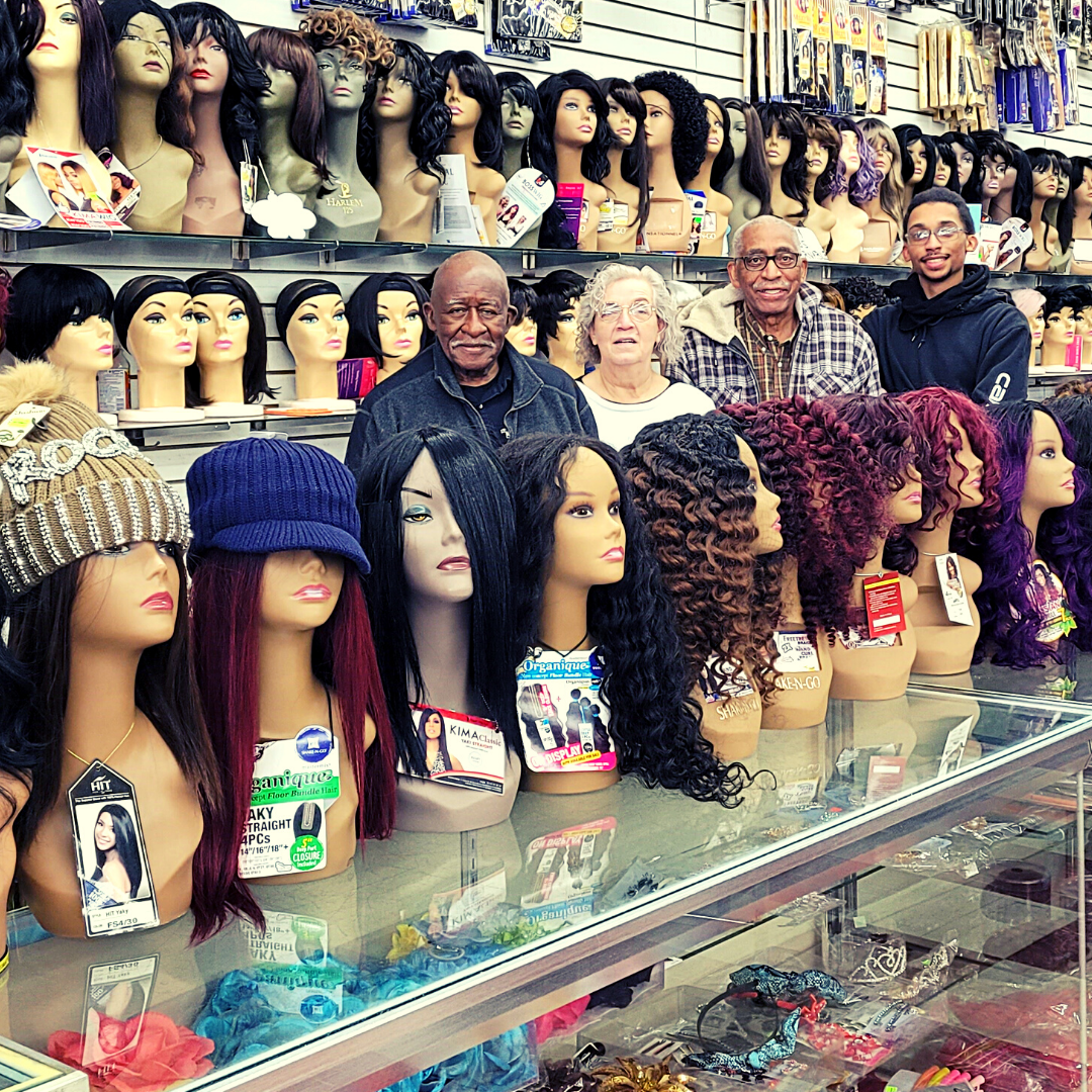 Jet Beauty Mart owners and employees standing behind a row of their wigs for sale