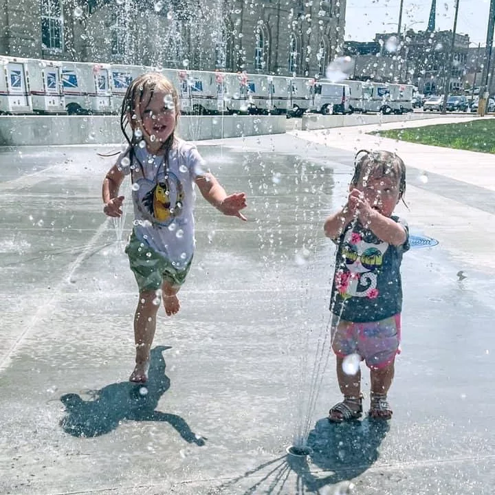 two young girls are playing in a fountain at the Freeport Art Plaza splash pad